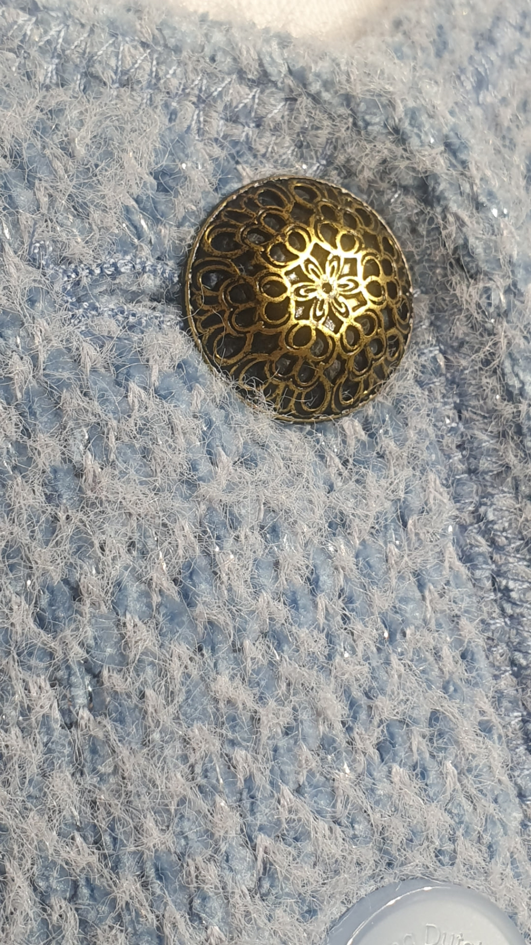 Close-up of an ornate gold button on a sky-blue textured jacket